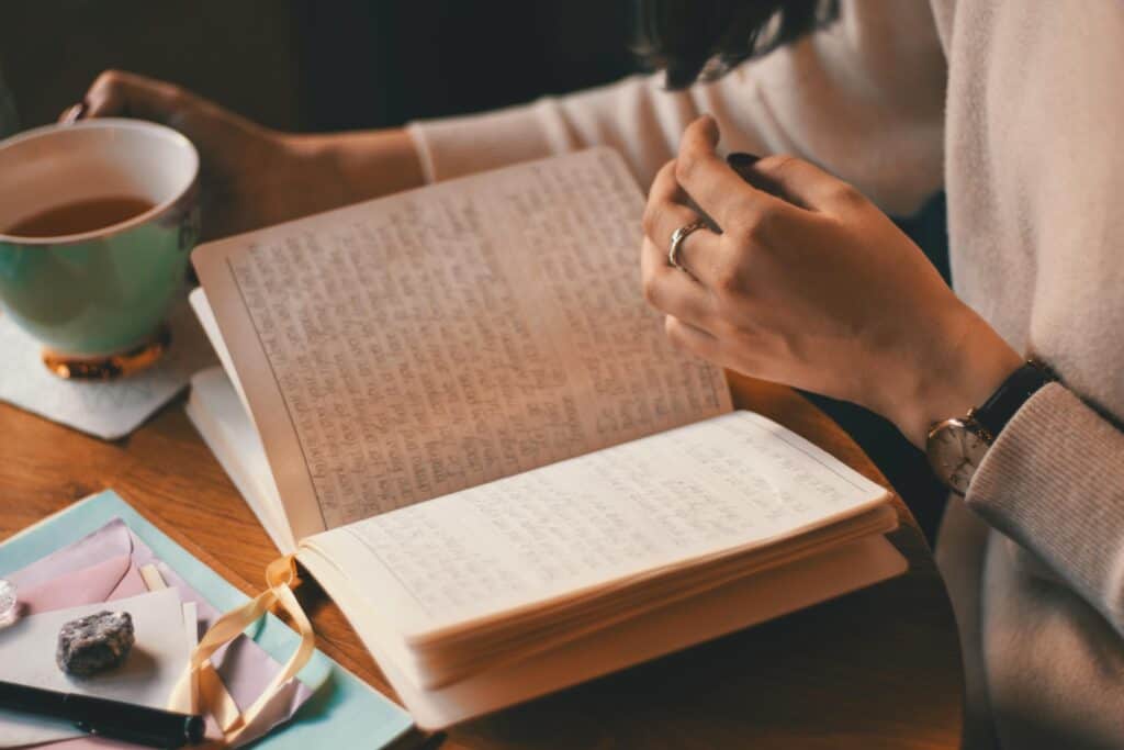 woman sitting at table ready a book and drinking coffee